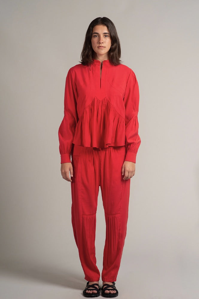 Una mujer viste la blusa Montería roja de manga larga hecha de cupro y un pantalón rojo de corte recto con plisados de la marca Yakampot, moda mexicana que combina técnicas ancestrales con diseño contemporáneo
